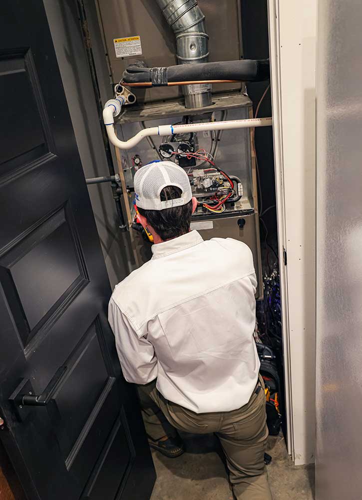 Tech servicing the inside split unit wearing hat and white shirt.