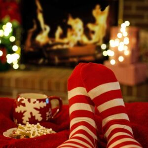 someone with red and white striped socks resting their feet in front of a fireplace by a christmas mug